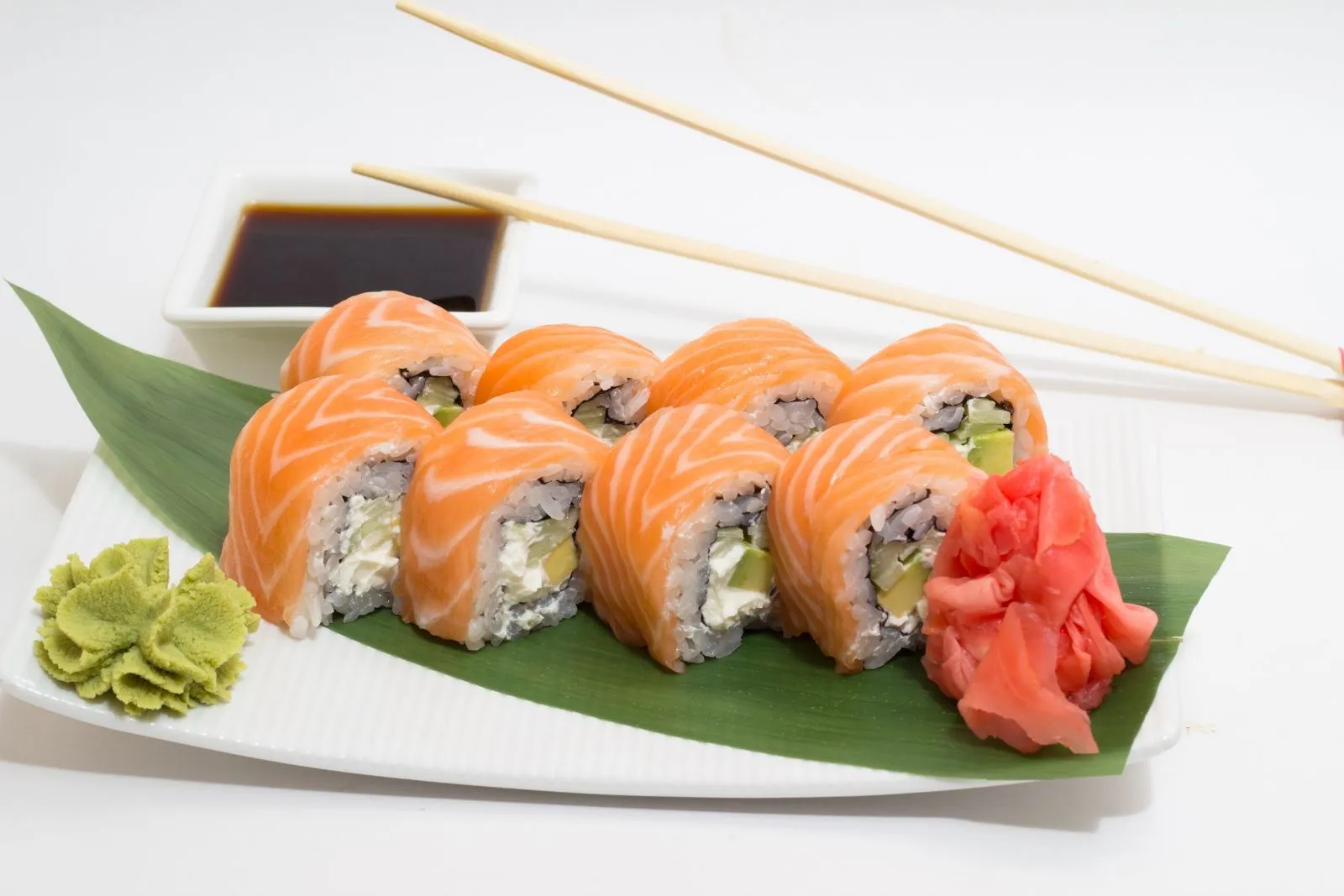Salmon sushi rolls served on green leaf with pickled ginger, wasabi and soy sauce